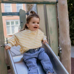 op deze afbeelding zie je een klein meisje die van een glijbaan afgaat in een hele leuke fashion outfit. Deze trui wordt verkocht op deze webshop. De gestreepte trui van La Oliva Kids in 100% katoen